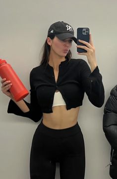 a woman taking a selfie with her cell phone while wearing a hat and leggings