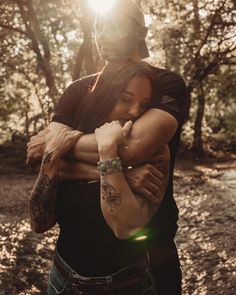 a man and woman hugging in the woods with sun shining through trees on their backs