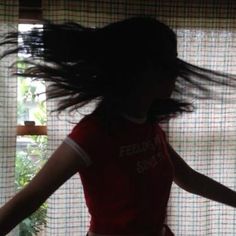 a woman is standing in front of a window with her hair flying through the air