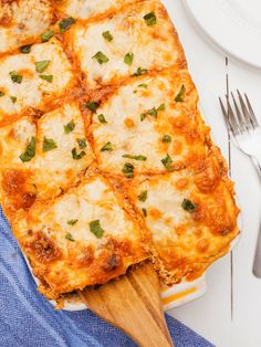 a square casserole with cheese and green onions on a blue towel next to silverware