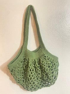 a green crocheted bag hanging on the wall next to a white wall,