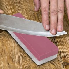 a person holding a knife on top of a block of pink paper next to a knife sharpener