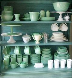 a green china cabinet filled with dishes and cups