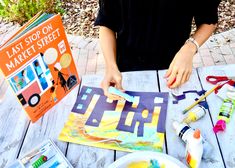 a person sitting at a table with some art supplies and books on top of it