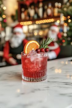 a red drink with orange slice and rosemary garnish on the rim sitting on a marble counter