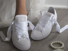 a pair of white shoes with pearls on the floor next to a bride's dress