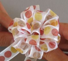 a hand holding a white and yellow polka dot hair bow