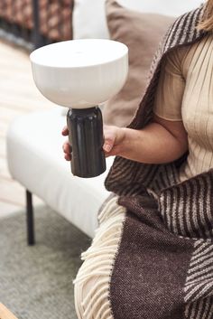 a woman sitting on a couch holding a coffee cup in her hand while wearing a sweater