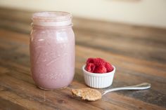 a glass jar filled with raspberry smoothie next to a bowl of raspberries