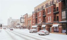 cars are parked on the street in front of buildings and snow covered sidewalks, during a winter storm