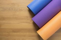 three yoga mats stacked on top of each other in front of a wood flooring surface