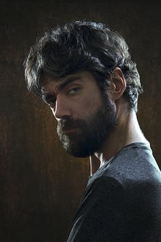 a man with long hair and beard standing in front of a wall