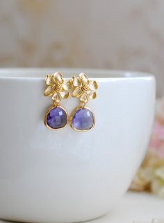 Stunning amethyst purple glass jewels and gold flowers post earrings. Sparkly glass jewels are faceted and gold framed. Flowers are matte gold plated over brass with sterling silver ear posts that are great for sensitive skin. These earrings are perfect for a romantic night out or a gold and purple themed wedding.Arrives in gift box.Measurement & Details:Total length: approx. 1.2" (29mm)Purple jewels: 13mm x 15mmEar wires: 925 sterling silver post, hypoallergenic.For more beautiful modern ea Gold Amethyst Jewelry For Anniversary, Elegant Lavender Flower Earrings For Gift, Elegant Purple Sterling Silver Flower Earrings, Elegant Purple Flower Shaped Earrings, Elegant Purple Flower Earrings, Gold Flower Shaped Jewelry With Gemstone, Gold Flower Gemstone Jewelry, Gold Flower-shaped Gemstone Jewelry, Flower Shaped Amethyst Jewelry For Anniversary