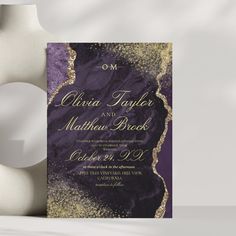 a purple and gold wedding card with the word om written on it next to a vase