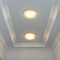 two lights that are on the ceiling in a room with white walls and trimmings