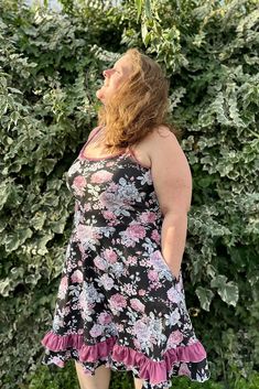 a woman standing in front of a bush wearing a black and pink dress with flowers on it