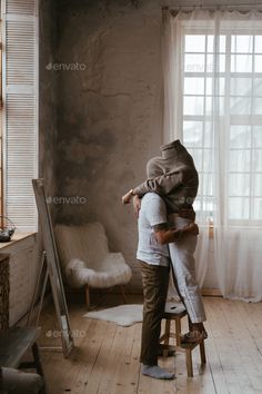 a man and woman hug in the corner of their living room while they look out the window