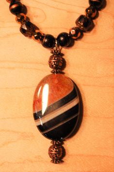 My husband and I designed and handmade this lovely one-of-a-kind beaded necklace.  The beads are semi-precious gemstone, crystal, and copper tone metallic, and the pendant is a beautiful orange, black, and cream agate.  And, the pendant is reversible - the reverse side is black and cream.   This necklace measures 22 inches in length, and the agate pendant measures an additional 2.5 inches.  It has a toggle clasp. Ours is a non-smoking home. Round Onyx Beaded Necklaces For Gifts, Round Onyx Beaded Necklace As A Gift, Round Onyx Beaded Necklace For Gift, Gift Onyx Beaded Necklaces, Onyx Beaded Necklaces With Round Beads For Gifts, Onyx Beaded Necklace With Round Beads As Gift, Agate Black Beads Necklace As Gift, Agate Black Beads Necklace For Gift, Agate Necklace With Black Beads As A Gift