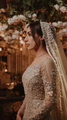 a woman in a wedding dress and veil looking off to the side with flowers hanging from the ceiling behind her