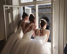 two women in white dresses are looking out the window