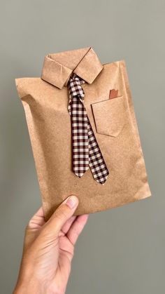 a hand holding a brown paper bag with a tie on it and a pocket for the shirt