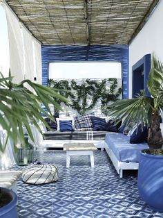 a living room filled with lots of blue furniture and potted plants on top of it