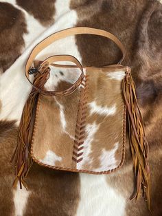 a brown and white spotted cowhide bag with tassels on the handle is laying down