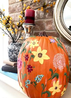 an orange painted pumpkin sitting on top of a mantle next to a mirror and flowers