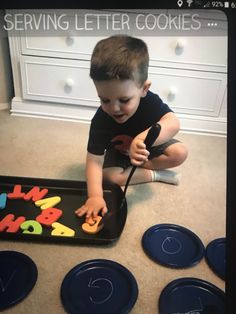 a young boy sitting on the floor in front of a tray with letters and numbers