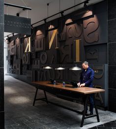 a man sitting at a table in front of a large wall with letters on it