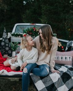 a mother and her daughter sitting on a blanket in the back of a truck with christmas decorations