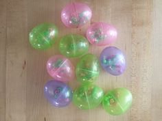 several plastic easter eggs sitting on top of a wooden table with green and pink decorations