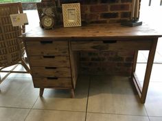 a wooden desk with two chairs and a clock on it's shelf next to a brick wall