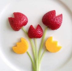 three strawberries and two orange slices on a white plate with green stems in the shape of hearts