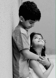 a boy and girl standing next to each other near a wall with their arms around one another