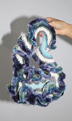 a hand holding up a crocheted object in the shape of a spiral design