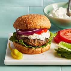 a burger with lettuce, tomato and onion on a plate next to a bowl of sour cream