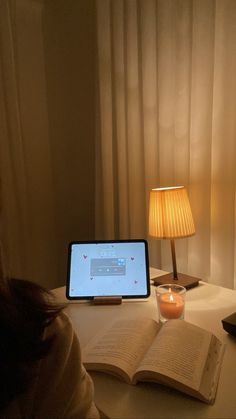 a woman sitting at a desk with an open book and a tablet computer on it