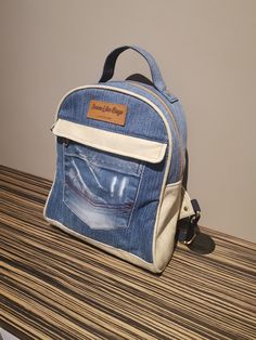 "Denim Backpack. From daily life to commuting to work, this Denim Backpack has your back. A large zipped compartment offers room for books and an extra slot for keeping your laptop secure. There is an exterior pocket that is clipped by two buttons in the front to help keep electronics and small essentials stored. As well the bag has two smaller pockets on either side to keep smaller items. Product Size: Width 13cm (5\"), Length 25cm (10\"), Height 30cm (12\")." Denim Backpack For Everyday And Back To School, Everyday Denim Backpack For Back To School, Daily Denim Backpack, Travel Denim Backpack, Denim Blue Standard Backpack With Zipper, Denim Backpack For Back To School, Denim Travel Backpack, Denim Blue Backpack With Zipper Closure, Everyday Denim Standard Backpack