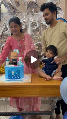 a man and woman standing next to a baby in front of a cake on a table