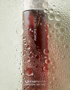 a bottle of red liquid sitting on top of a window sill covered in water droplets