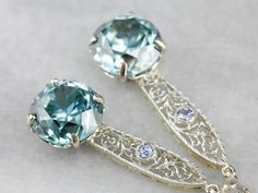 "Handcrafted in our New Hampshire studio, these earrings represent both something old, and something blue! The drops have been converted from an early 1900's era bar pin, set with light blue sapphires, and the filigree provides a pretty cobweb motif and gives length to the sparkling blue zircon gemstones we've set below. Metal: 14K White and Yellow Gold Gem: 2 Blue Zircon totaling 17.28 Carats Gem Measurements: 11 mm, Round Accents: 2 Sapphire totaling .14 Carats Earrings Length: 47 mm Earrings Heirloom Wedding Earrings Pierced, Vintage Gemstone Earrings For Formal Occasions, Art Deco Gemstone Earrings For Gift, Vintage Drop Earrings With Prong Setting, Heirloom Style Wedding Earrings With Intricate Design, Heirloom Wedding Earrings With Intricate Design, Blue Art Deco Wedding Earrings, Silver Gemstone Art Deco Earrings, Fine Jewelry Filigree Earrings For Wedding