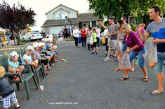 a group of people sitting on top of green chairs in front of a street filled with parked cars