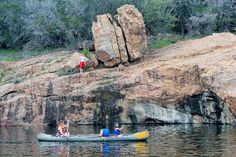 three people are in a canoe on the water near some large rocks and trees,