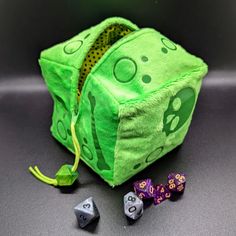 a green dice bag with skulls and bones on it next to two dice holders that are purple and yellow