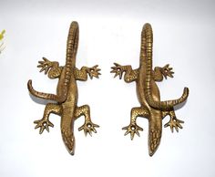 two gold colored lizards sitting next to each other on a white surface with flowers in the background