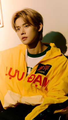 a young man sitting on top of a couch wearing a yellow jacket