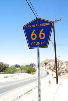 a blue and yellow street sign sitting on the side of a road next to power lines