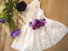 a white dress with purple flowers on it next to a bouquet of green and purple flowers