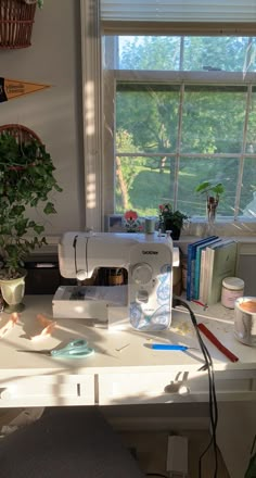 a sewing machine sitting on top of a white table next to a plant and books